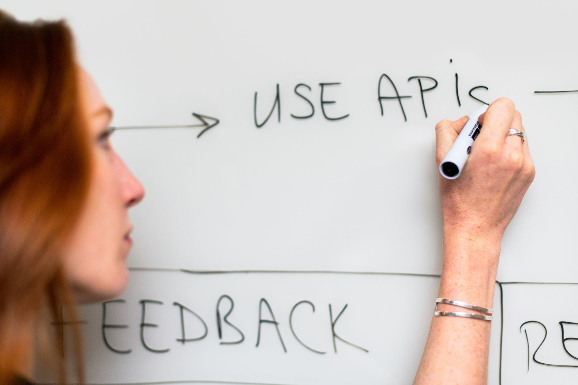 Woman writing on a white board 'use APIs'